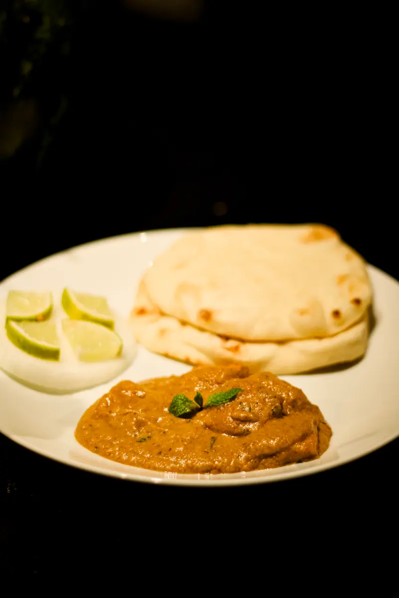 Naan with curry and lime, plated on a dark table