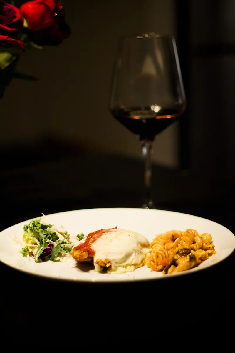 A plated dish with greens beside a glass of red wine